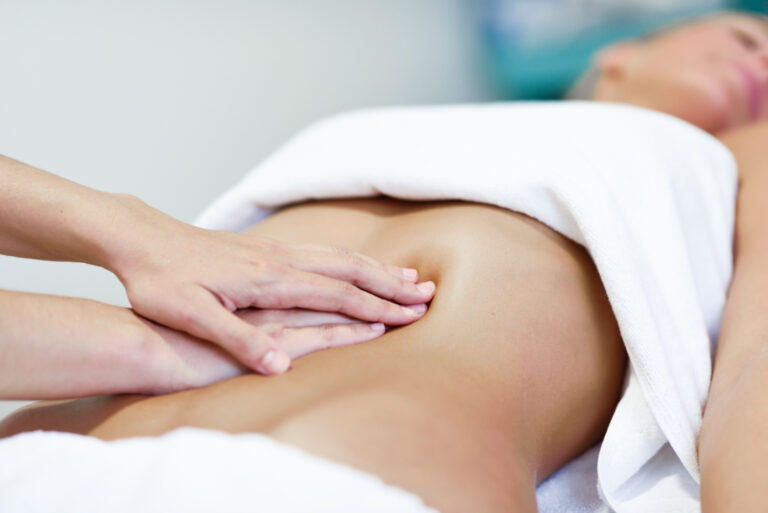 Manos realizando un masaje en el abdomen de una persona tumbada